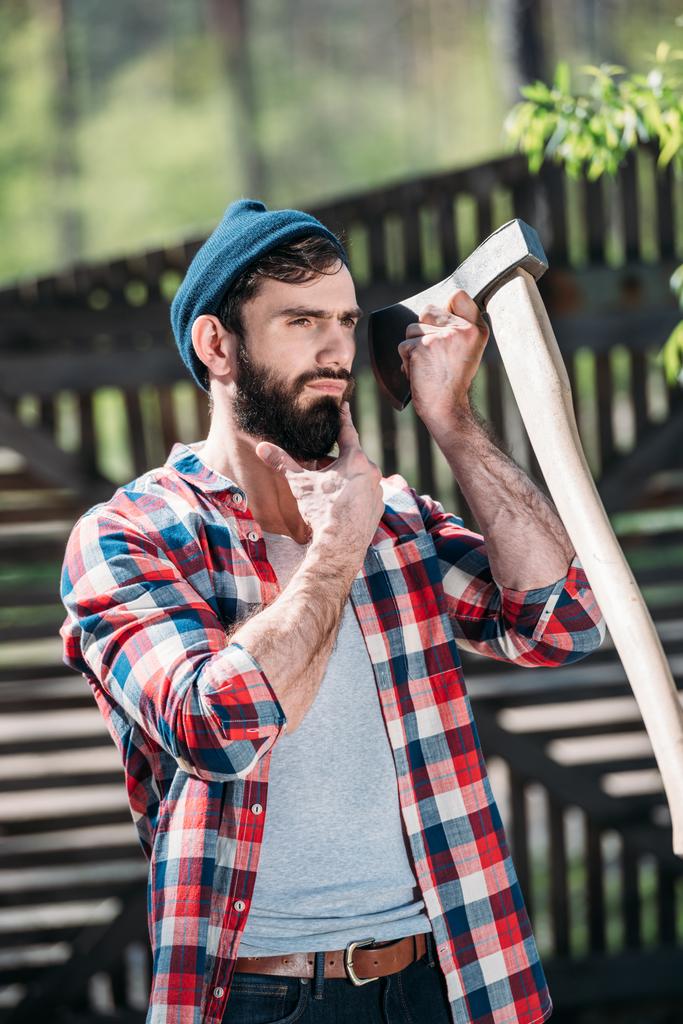 ξυλοκόπος σε καρώ πουκάμισο ξύρισμα γενειάδα από τσεκούρι στο πριονιστήριο  - Φωτογραφία, εικόνα
