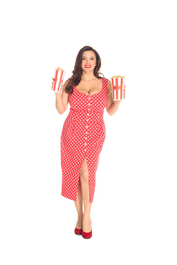 glimlachend plus grootte vrouw in rode jurk met dozen van popcorn geïsoleerd op wit - Foto, afbeelding