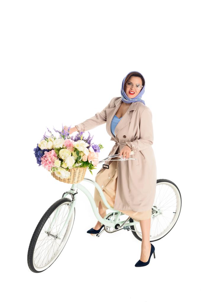 Вид в полный рост стильной женщины в пальто и туфлях на высоком каблуке, сидящей на велосипеде и улыбающейся камере на белом фоне
 - Фото, изображение