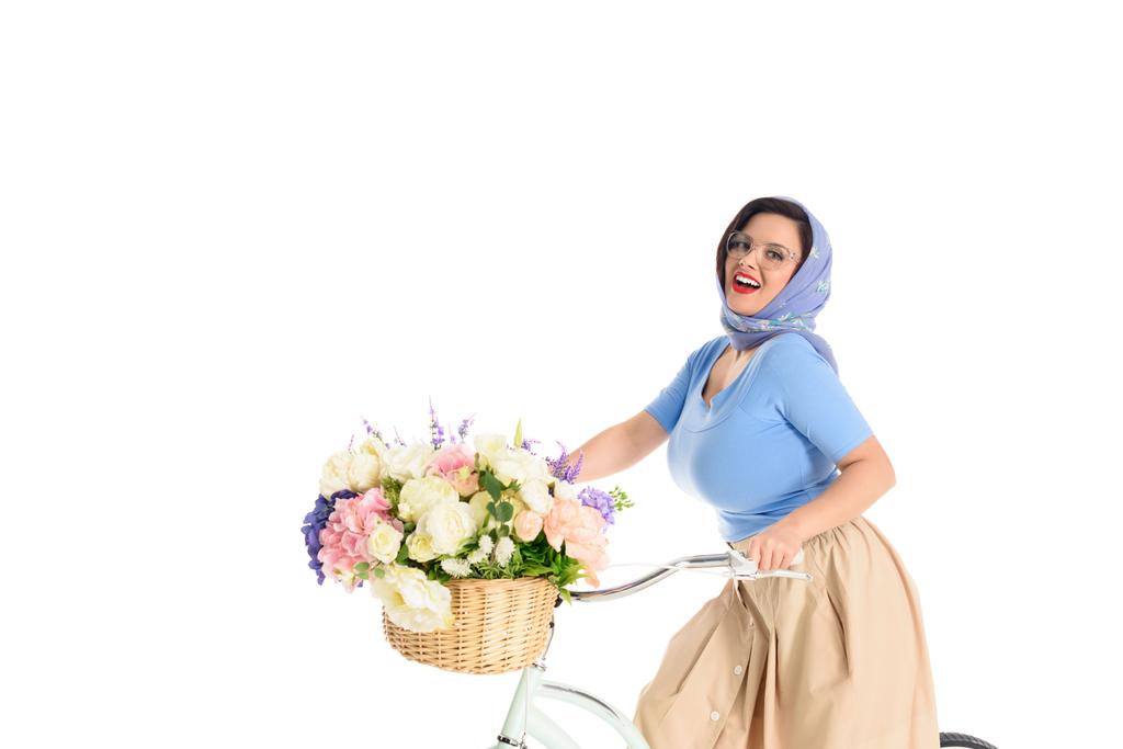 beautiful young pin up woman sitting on bike with flower basket and smiling at camera isolated on white - Photo, Image