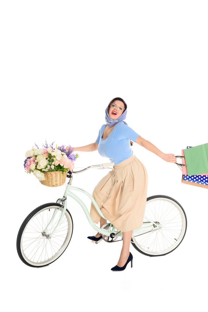 happy pin up woman with shopping bags riding bicycle and smiling at camera - Photo, Image