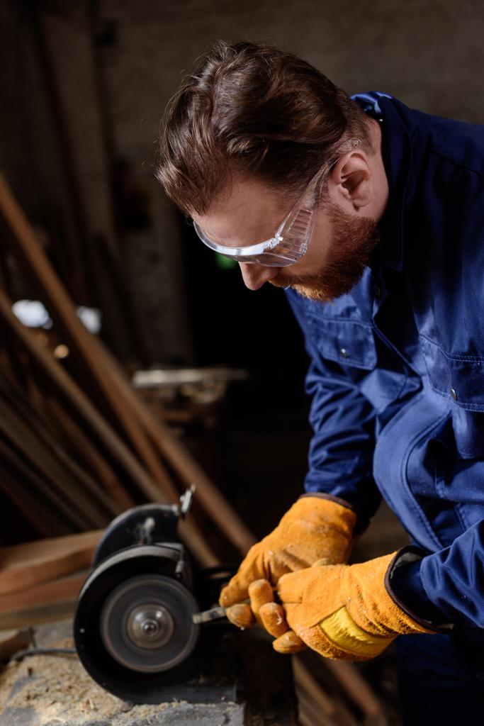 travailleur dans les lunettes de protection et les gants à l'aide d'une rectifieuse à la scierie
 - Photo, image