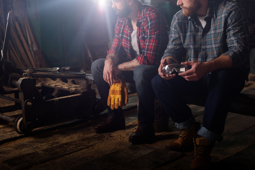 обрезанный снимок двух рабочих, держащих защитные перчатки и гуглы на лесопилке
  - Фото, изображение