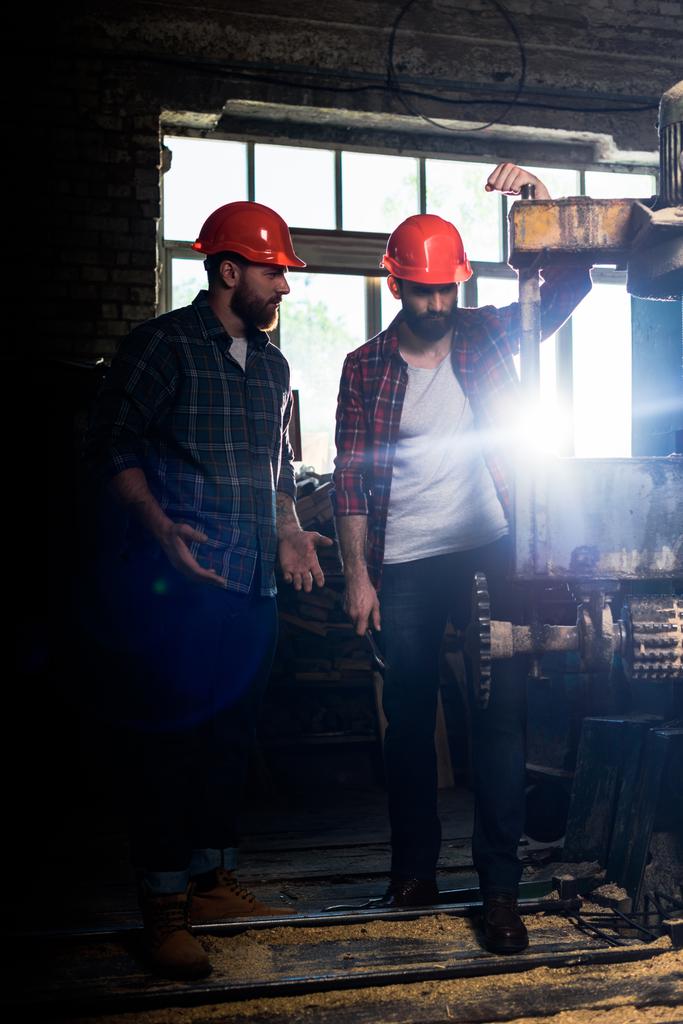 iki işçi Koruyucu baretler kereste fabrikası makine aleti kullanarak sakallı  - Fotoğraf, Görsel
