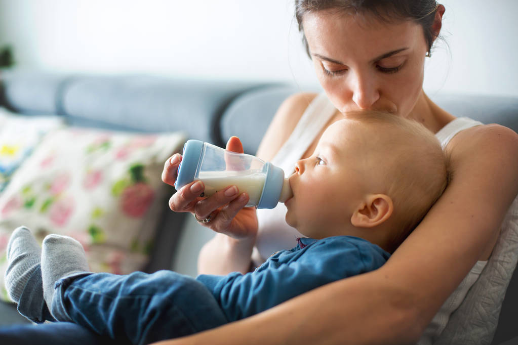 Матері, годування її хлопчика з пляшки, комфортно, сидячи на канапі в домашніх умовах - Фото, зображення