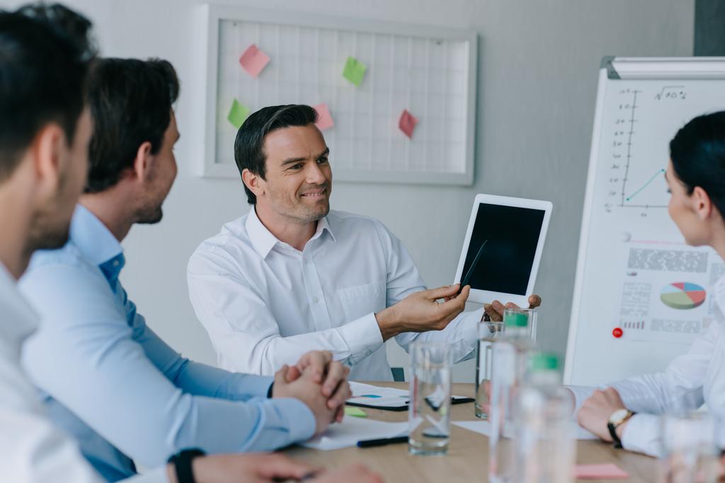Selektivní fokus podnikatel ukazuje na tabletu s černou obrazovkou při setkání s kolegy v kanceláři - Fotografie, Obrázek