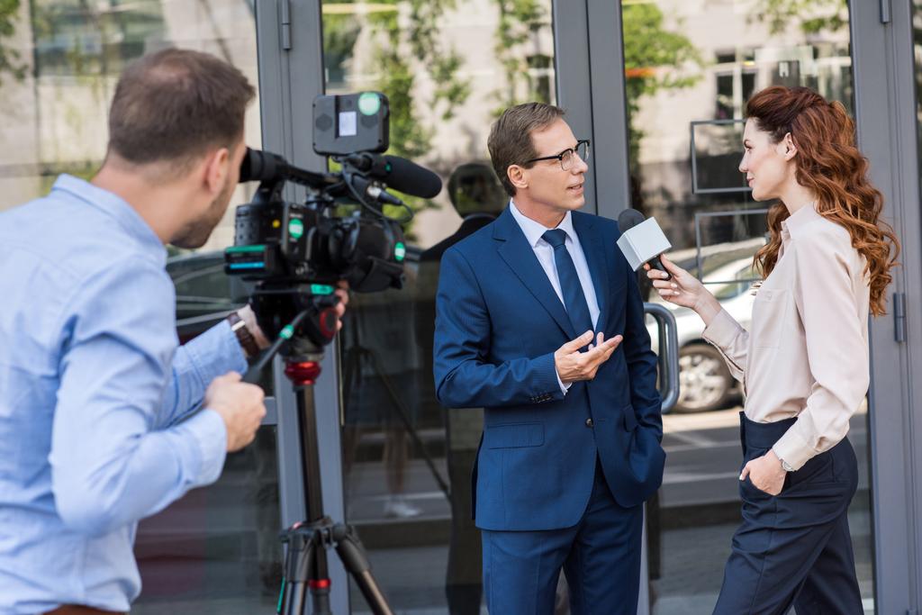 cameraman e reporter di notizie con microfono intervistando uomo d'affari vicino all'edificio per uffici
  - Foto, immagini