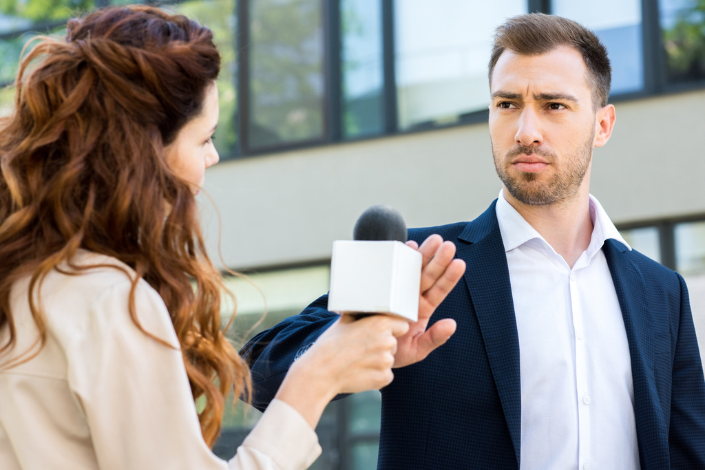 ankkurinainen, jolla on mikrofoni, kun vakava liikemies kieltäytyy haastattelusta
 - Valokuva, kuva