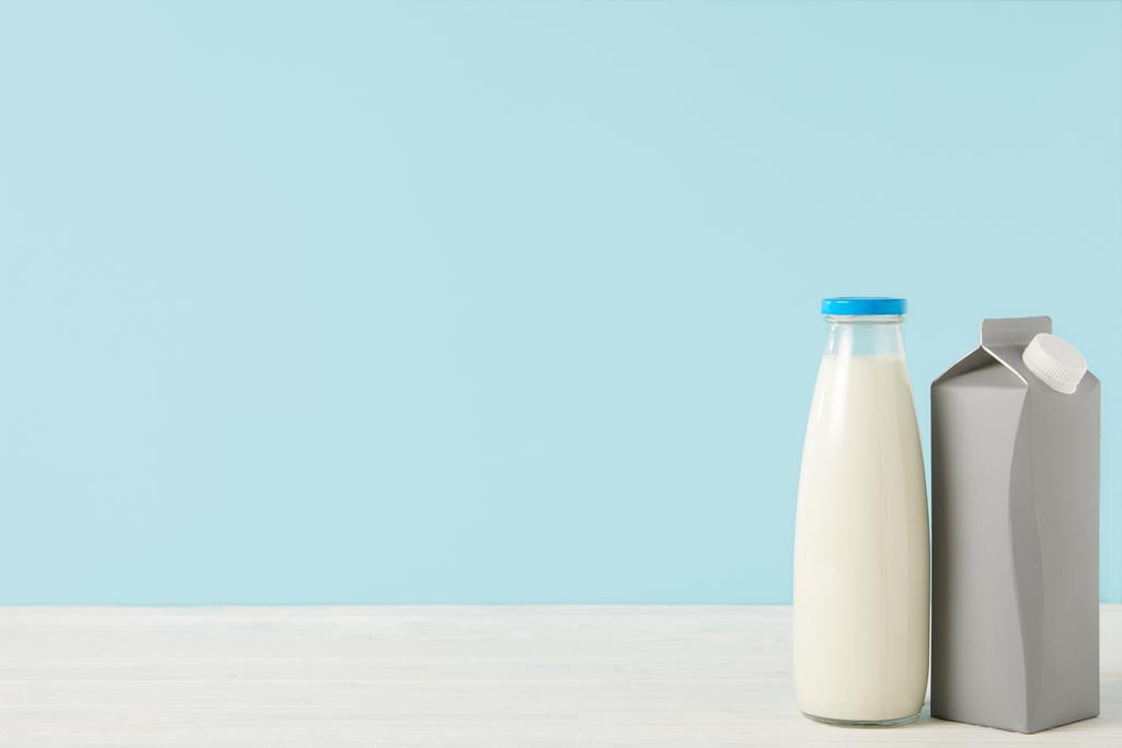 Nahaufnahme Bild der Milch in Flasche und leeren Karton Verpackung auf blauem Hintergrund  - Foto, Bild