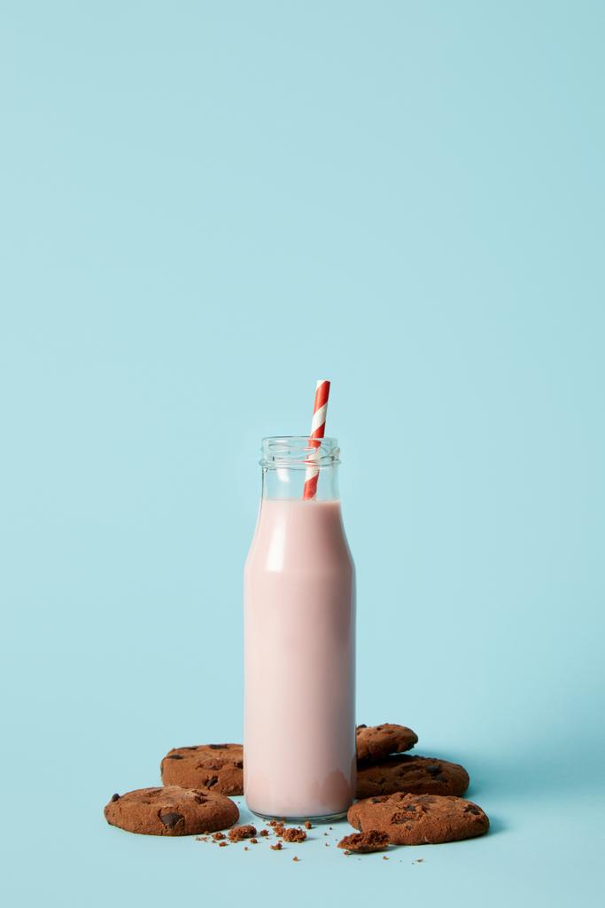 vista close-up de milkshake de morango em garrafa com palha de bebida cercada por biscoitos de chocolate no fundo azul
  - Foto, Imagem