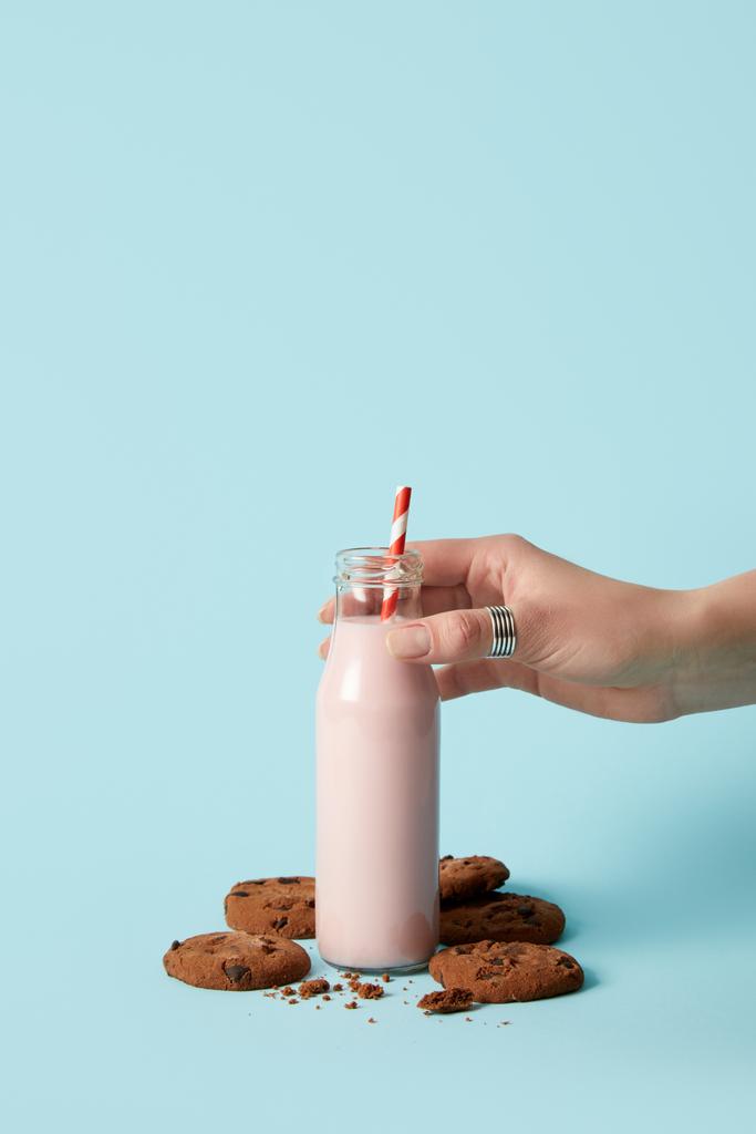 bijgesneden afbeelding van vrouw met fles met aardbei milkshake en chocolade koekjes op blauwe achtergrond  - Foto, afbeelding