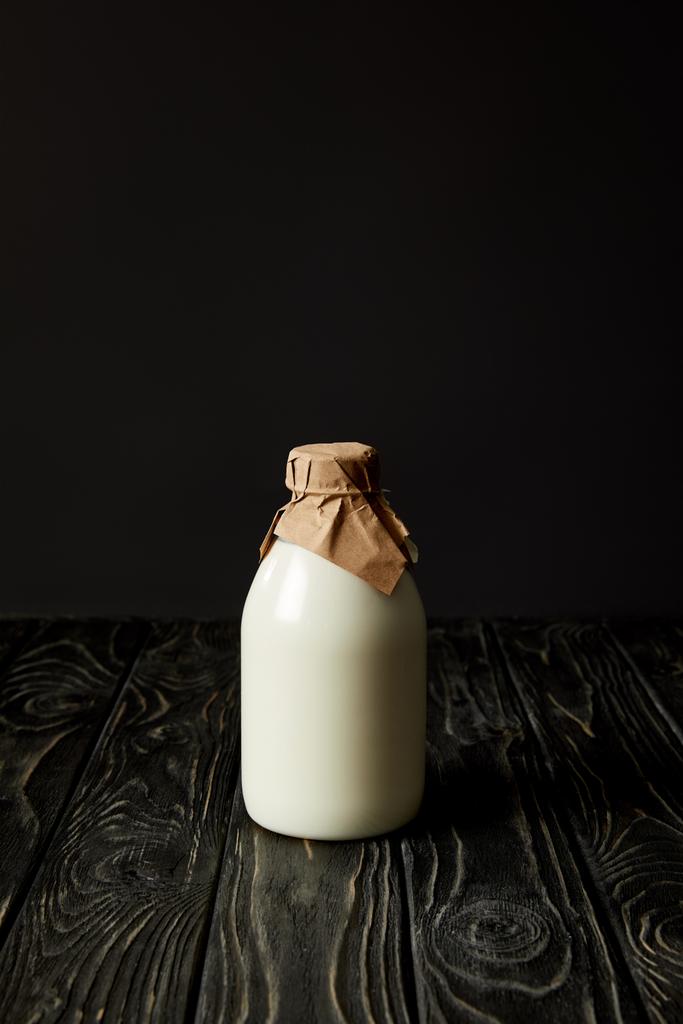 świeże mleko w butelce, zapakowane przez papier na czarnym tle  - Zdjęcie, obraz
