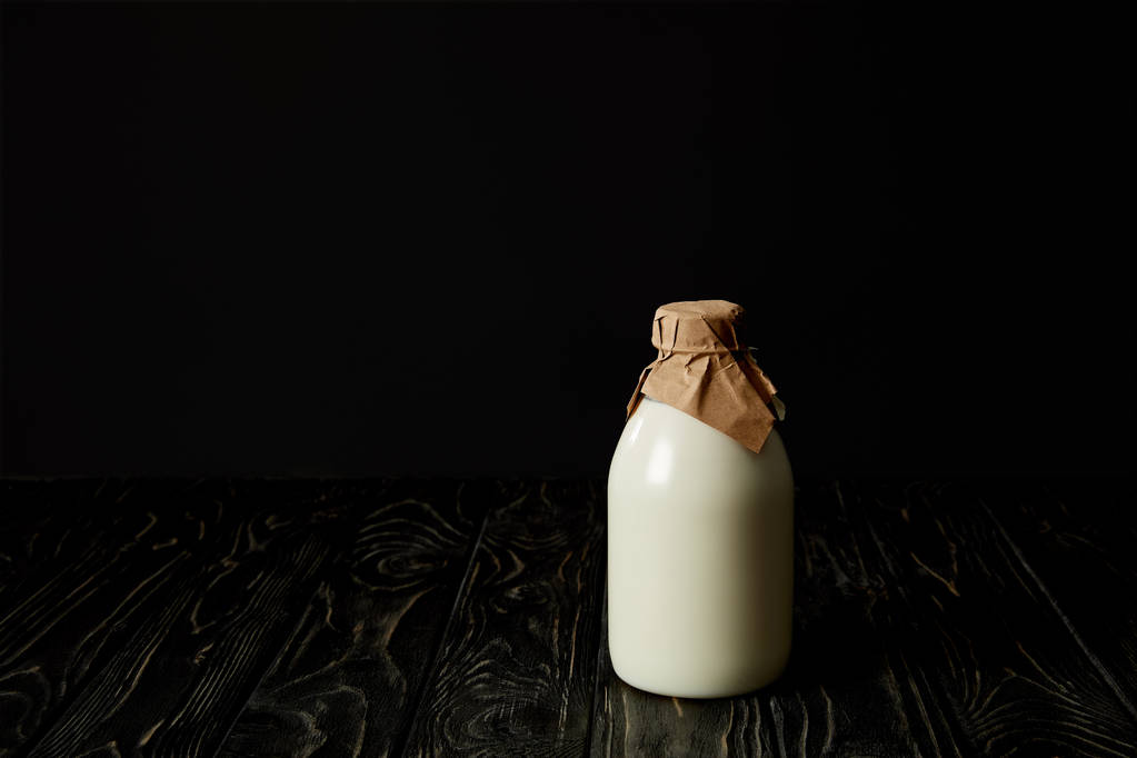 vista de cerca de la leche fresca en botella envuelta por papel sobre fondo negro
  - Foto, Imagen