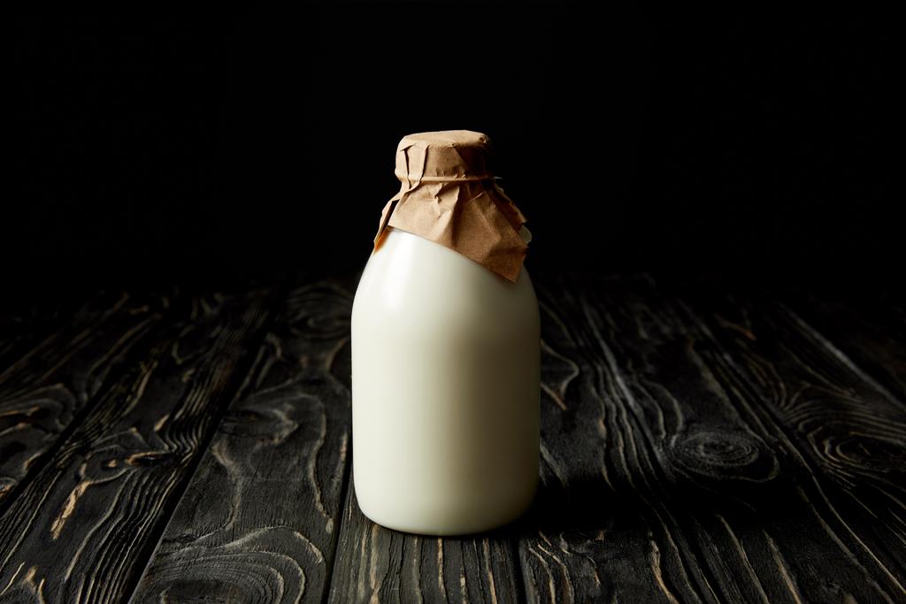 leche fresca en botella envuelta en papel sobre fondo negro
  - Foto, imagen
