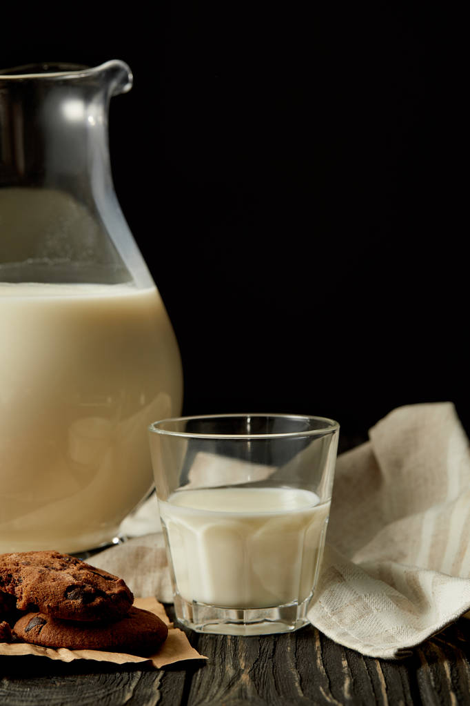 частковий вид на свіже молоко в глечику і склянці, шоколадне печиво та верескет на чорному тлі
  - Фото, зображення