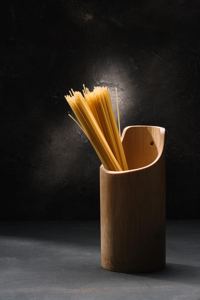 Bund rohe Spaghetti im Holzbehälter mit Knoblauch auf schwarzer Oberfläche - Foto, Bild
