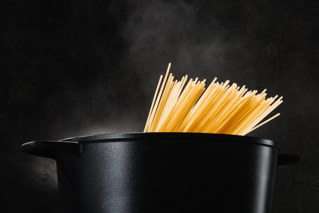 spaghetti koken in zwarte pan op donkere achtergrond - Foto, afbeelding