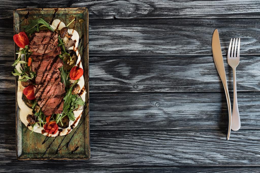 vue du dessus de délicieux steak rôti aux légumes et fourchette avec couteau sur table en bois
  - Photo, image