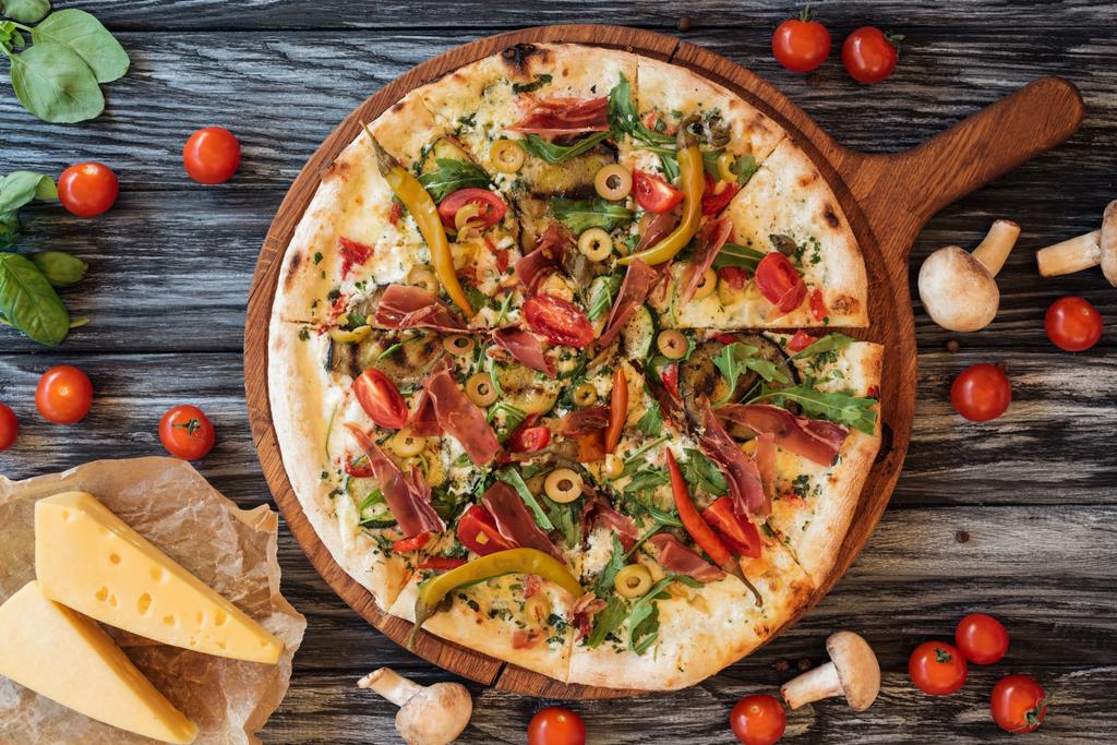 vista superior de la deliciosa pizza con verduras y carne en tabla de cortar de madera
  - Foto, imagen