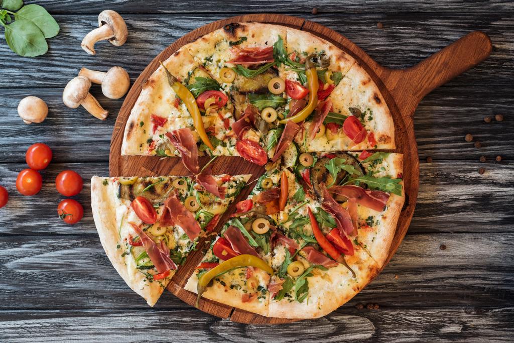 Gourmet-Pizza in Scheiben mit Gemüse und Fleisch auf einem Holzschneidebrett  - Foto, Bild