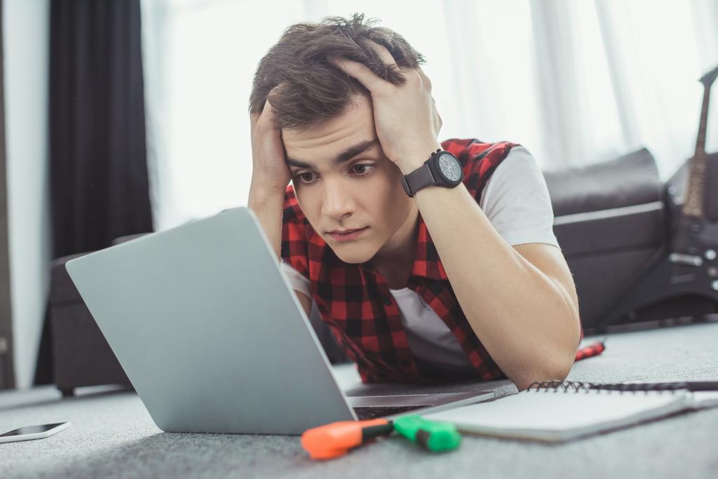 stressed teen boy studying with laptop while lying on floor - Photo, Image