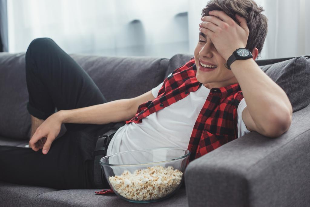 riéndose adolescente con palomitas de maíz viendo comedia película en casa
 - Foto, Imagen