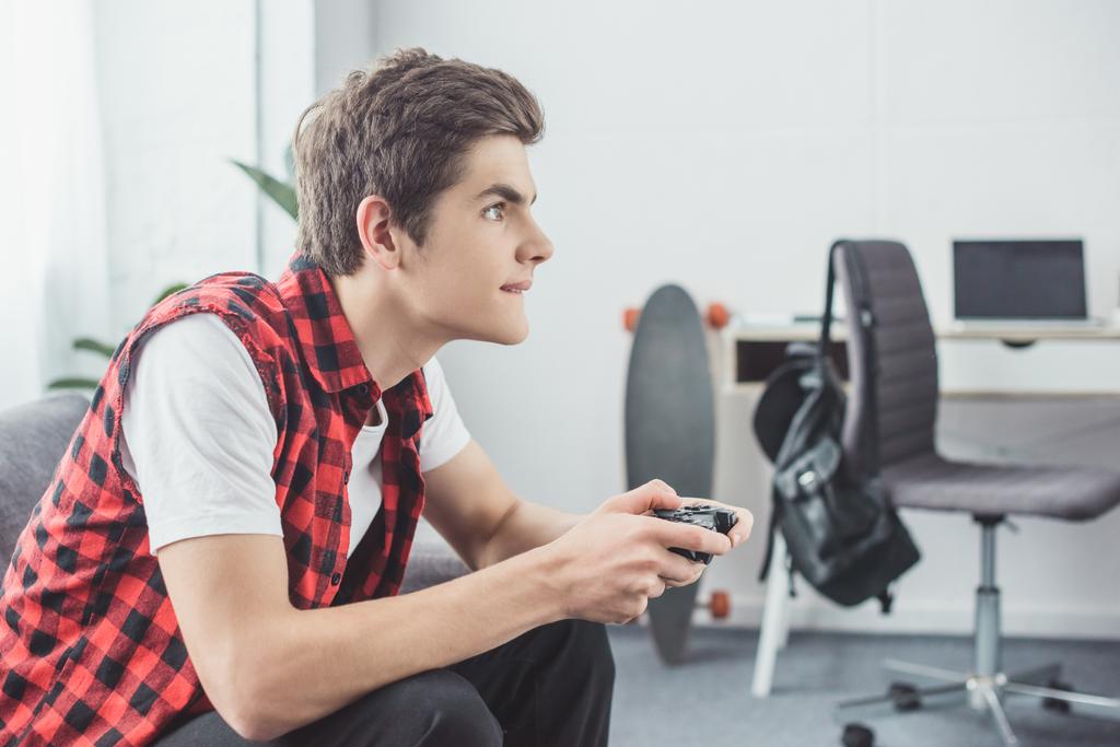 tiener jongen afspelen van video game met gamepad thuis - Foto, afbeelding