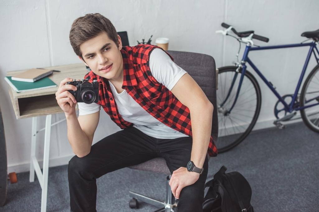 teenager with film camera sitting at home with bicycle behind - Photo, Image