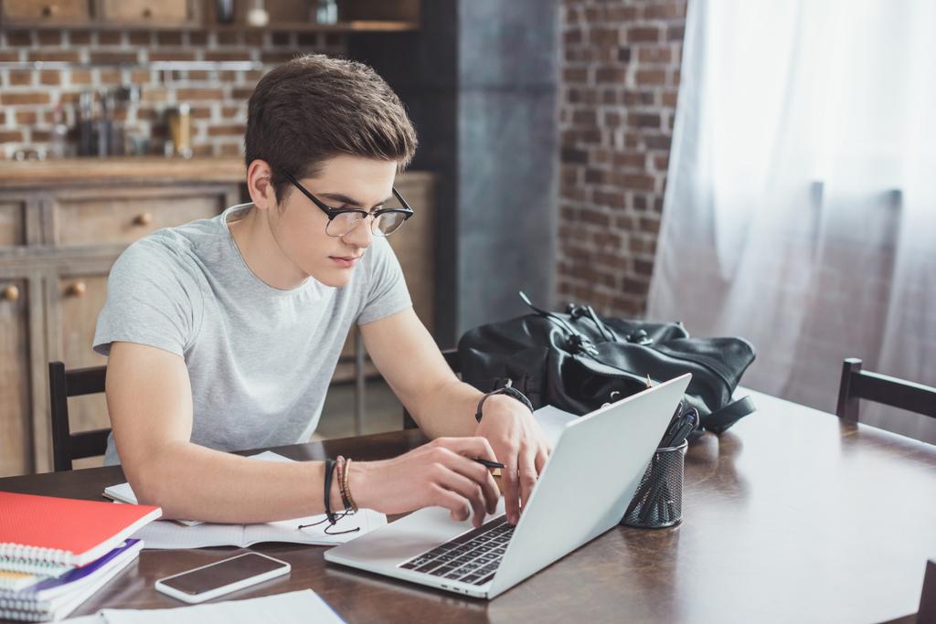 estudiante masculino haciendo la tarea y escribiendo en el ordenador portátil en casa
 - Foto, imagen