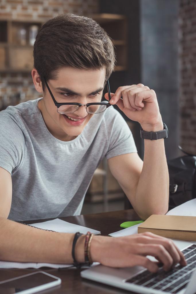 macho sonriente estudiante en gafas usando portátil en casa
 - Foto, imagen
