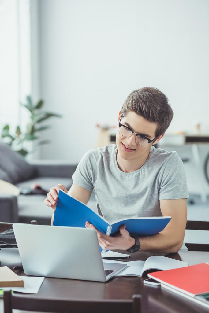 estudiante masculino haciendo deberes con copybooks y laptop en casa
 - Foto, imagen