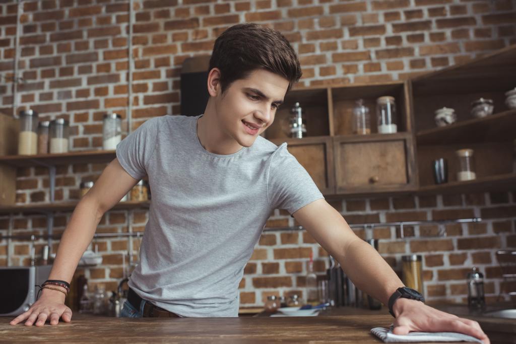 pěkný teen chlapec čištění tabulka s hadr v kuchyni - Fotografie, Obrázek