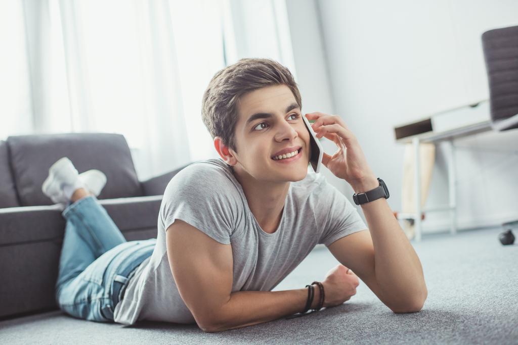 maschio sorridente adolescente parlando su smartphone mentre sdraiato sul pavimento
 - Foto, immagini