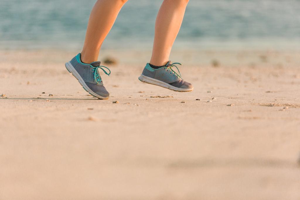 plan recadré de joggeuse en baskets courant sur une plage de sable fin avec la mer derrière
  - Photo, image