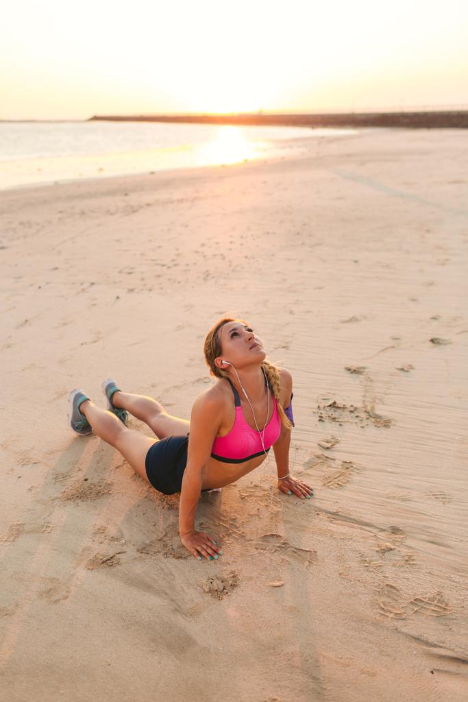 kulaklıklar içinde genç sporcumuz ile kum plajındaki egzersiz yaparak omuz çantası içinde smartphone  - Fotoğraf, Görsel