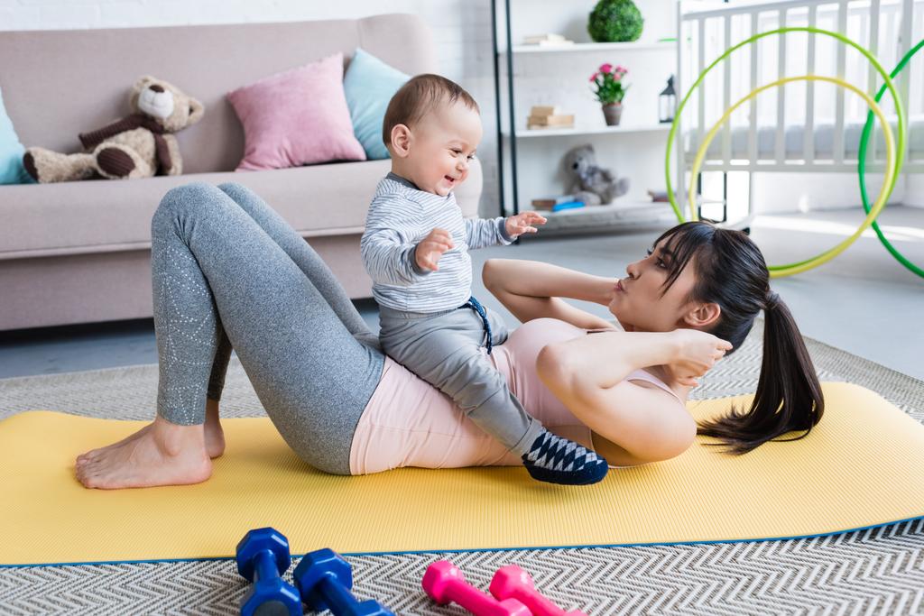 молодая красивая мать работает на коврике для йоги со своим маленьким ребенком дома
 - Фото, изображение
