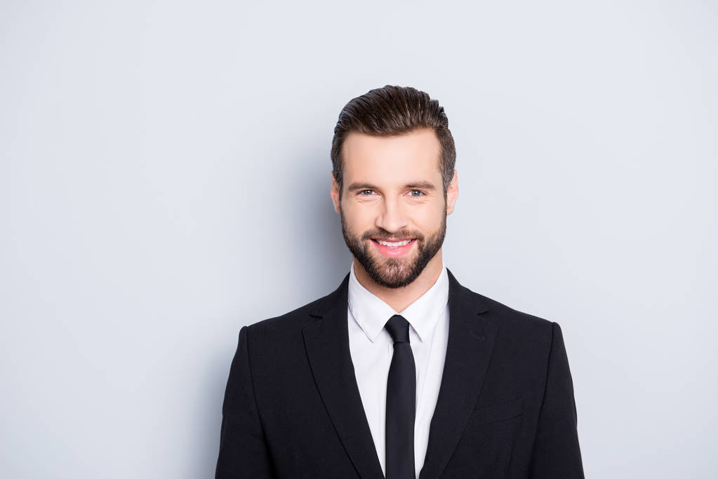 Porträt eines positiven, fröhlichen Geschäftsmannes mit moderner Frisur und elegantem Outfit, schwarzer Anzug mit Krawatte, der in die Kamera schaut, isoliert auf grauem Hintergrund - Foto, Bild