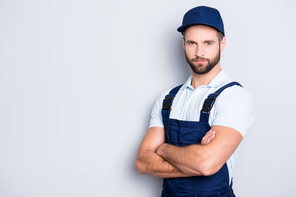 Portrait with copy space, empty place for advertisement of muscular half turned deliver in blue uniform looking ta camera, having his arms crossed, isolated on grey background - Photo, Image