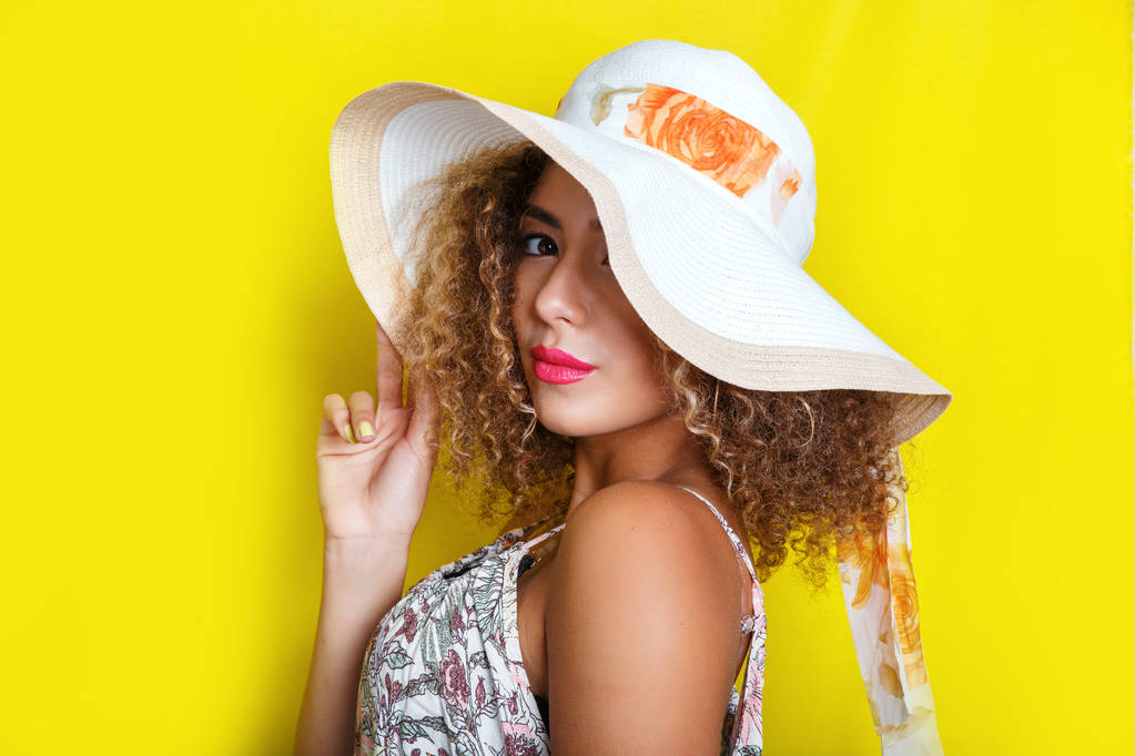 夏帽子でアフロの髪型を持つアフリカ系アメリカ人少女の美しさの肖像画。カメラ目線で黄色背景、ポーズの女の子. - 写真・画像