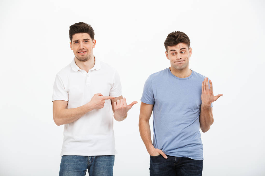 Porträt zweier verwirrter junger Männer, die vereinzelt mit dem Finger auf weißen Hintergrund zeigen - Foto, Bild