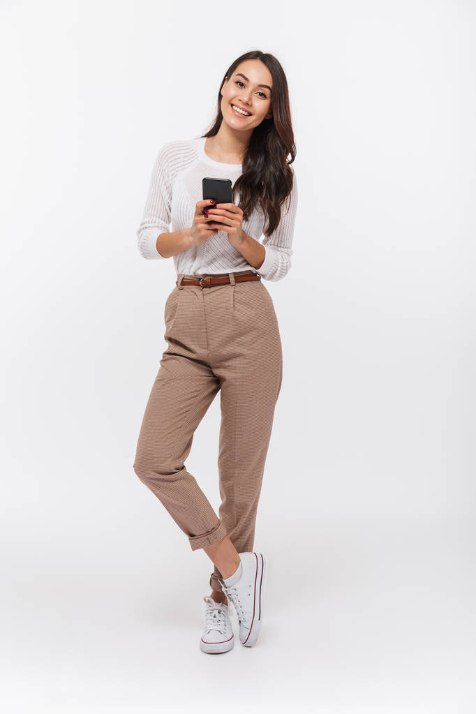 Volledige lengte portret van een gelukkig Aziatische zakenvrouw met behulp van de mobiele telefoon geïsoleerd op witte achtergrond - Foto, afbeelding