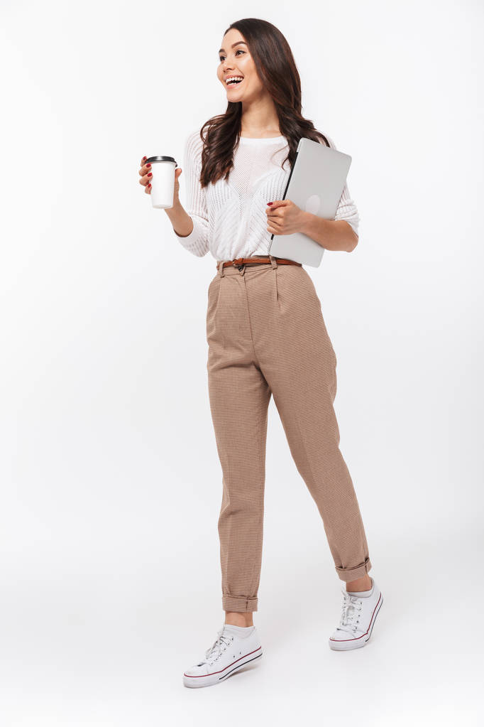 Ganzkörperporträt einer glücklichen asiatischen Geschäftsfrau, die Laptop und eine Tasse Kaffee to go bei sich trägt, während sie isoliert vor weißem Hintergrund läuft - Foto, Bild