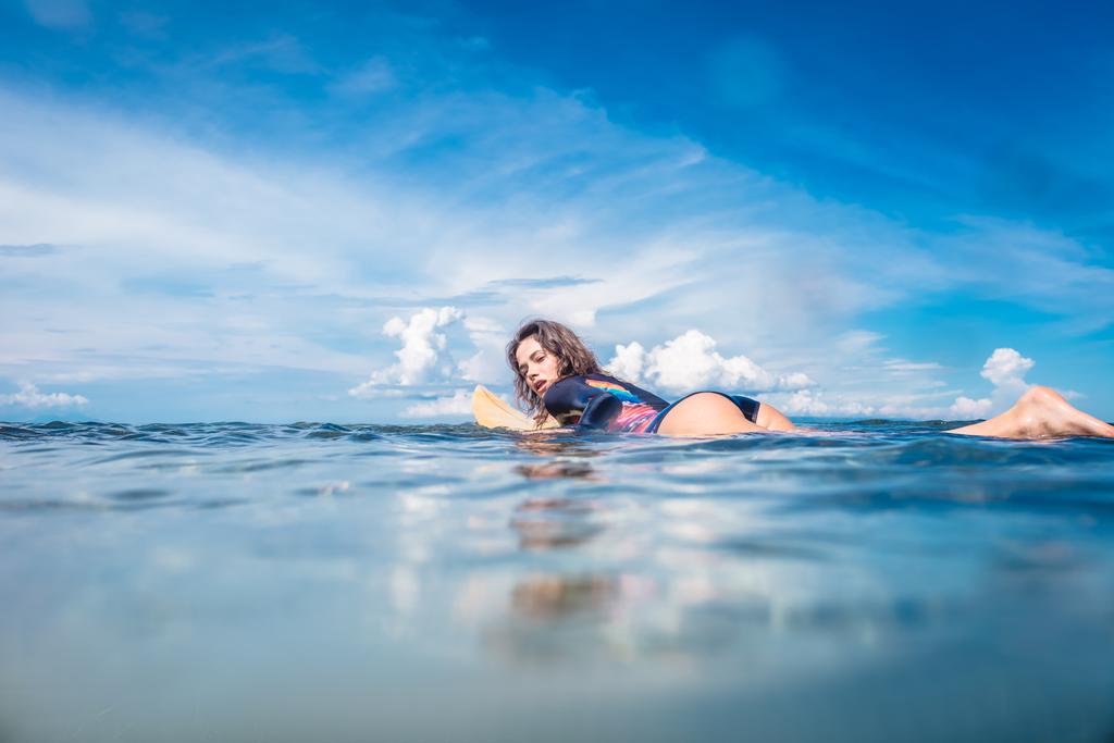 Вид сбоку молодой женщины в гидрокостюме на доске для серфинга в океане на пляже Нуса-дуа, Бали, Индонезия
 - Фото, изображение
