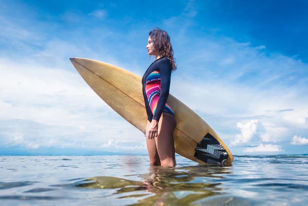 ヌサドゥア ビーチ、バリ、インドネシアの海でサーフィン ボードに立っているとウェット スーツで魅力的なスポーツウーマンの側面図 - 写真・画像