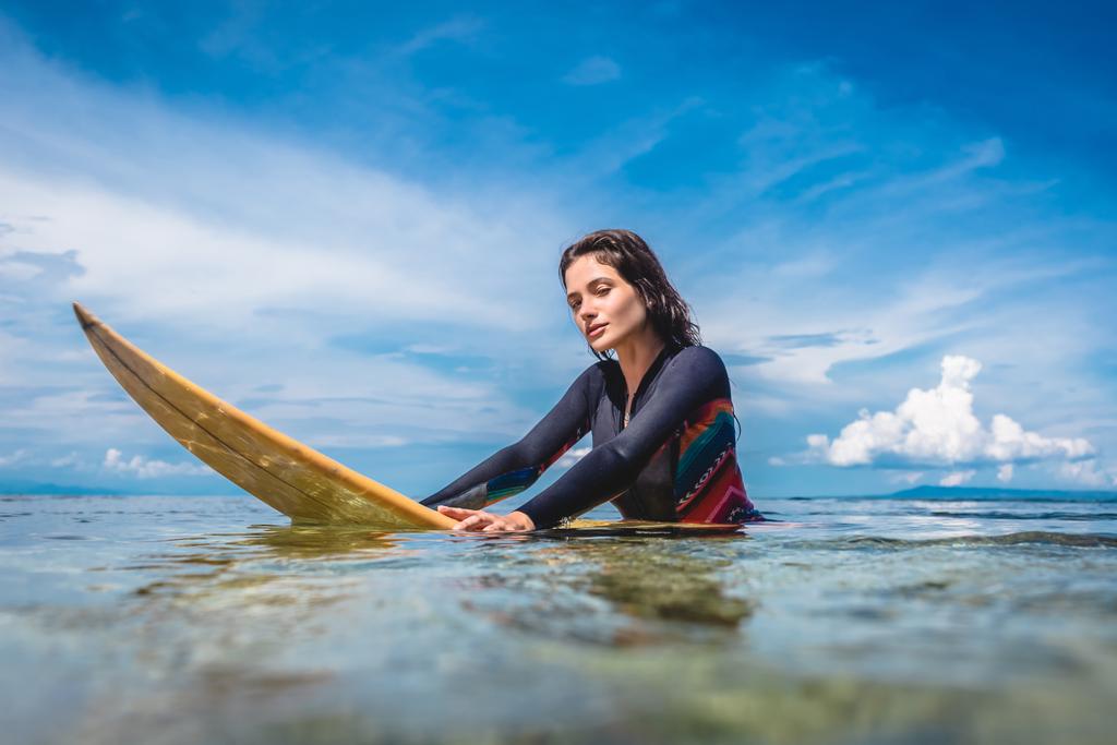 портрет молодой спортсменки в гидрокостюме на доске для серфинга в океане на пляже Нуса Дуа, Бали, Индонезия
 - Фото, изображение