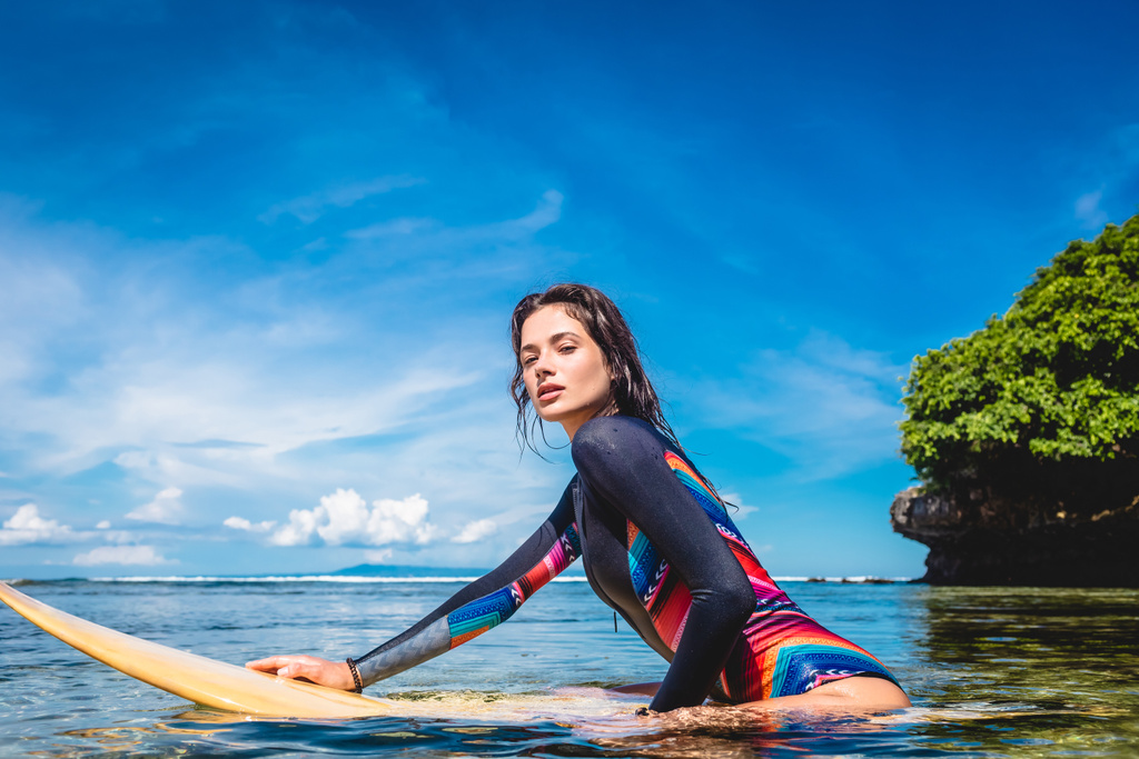 side view of pretty sportswoman in wetsuit on surfing board in ocean at Nusa dua Beach, Bali, Indonesia - Photo, Image
