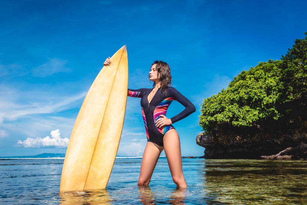 ヌサドゥア ビーチ、バリ、インドネシアの海でポーズのサーフボードとウェット スーツの魅力的な若い女性 - 写真・画像