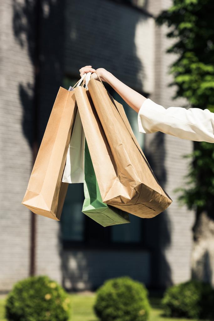 tiro cortado de mão feminina segurando sacos de compras na rua
  - Foto, Imagem