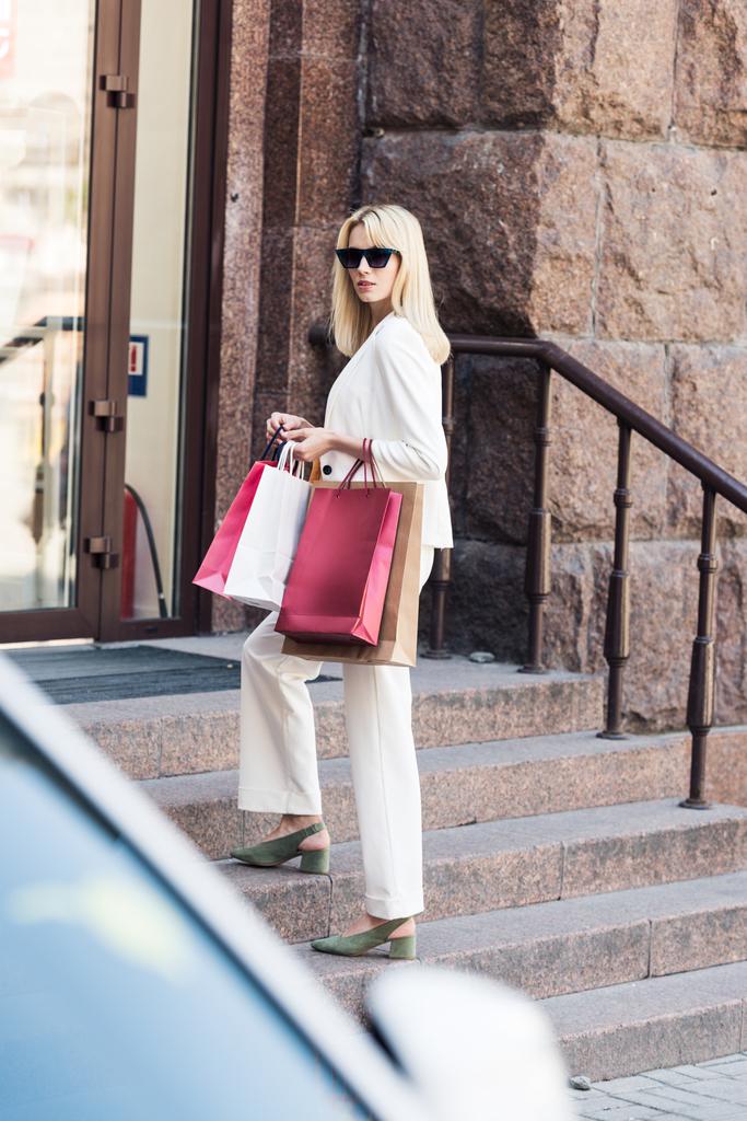 kaunis muodikas blondi nainen tilalla ostoskassit ja seisoo portaissa
 - Valokuva, kuva