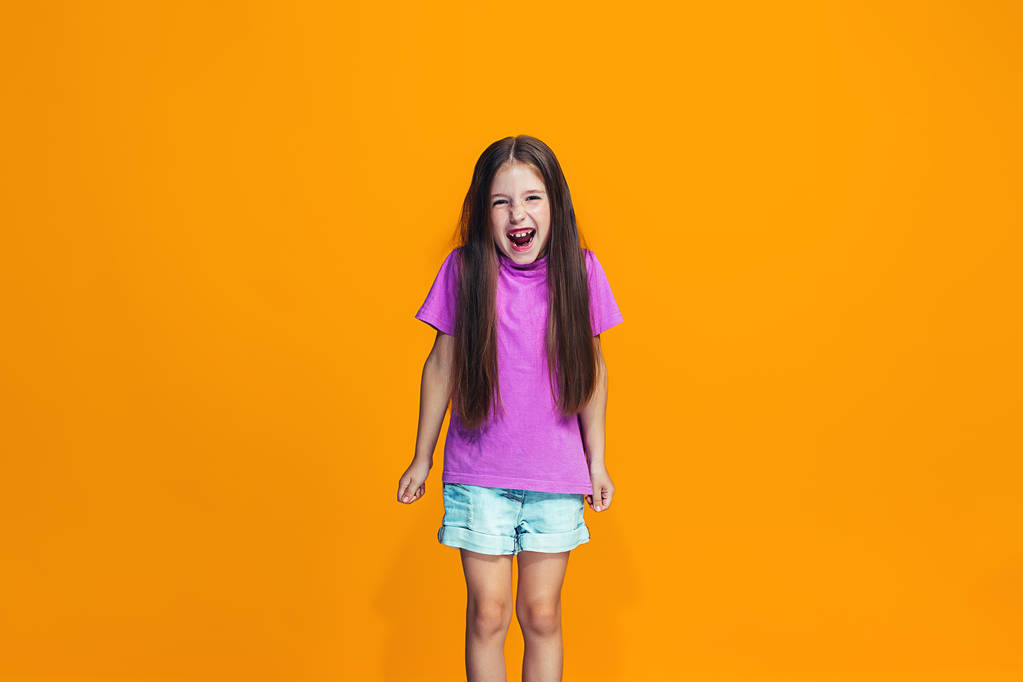 Šťastný dospívající dívka stojící a usmívá se proti oranžové pozadí. - Fotografie, Obrázek